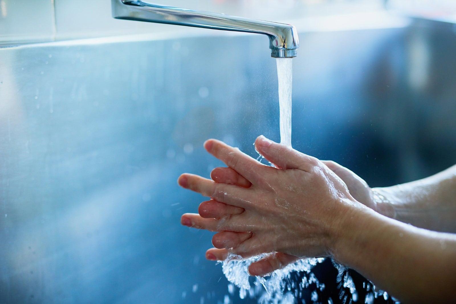 Man washing their hands under a large faucet