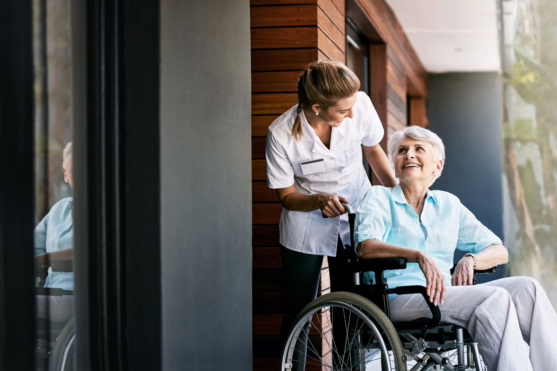 Senior women seated in a wheelchair being pushed by a nurse and smiling