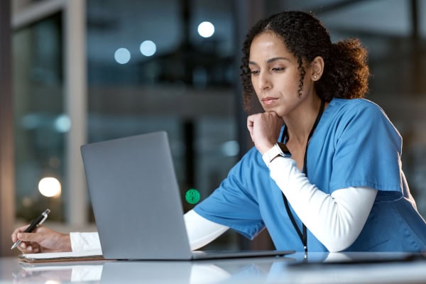 Healthcare professional working at laptop in deep thought.